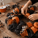 hands adding a pumpkin to a black and orange Halloween wreath with ribbon, mesh, and craft supplies