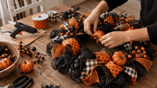 hands adding a pumpkin to a black and orange Halloween wreath with ribbon, mesh, and craft supplies