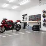 Red motorcycle in organized garage with tools, helmets, and jackets on wall-mounted pegboards