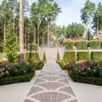 Brick pathway leading to ornate gate with lush garden and tall pine trees