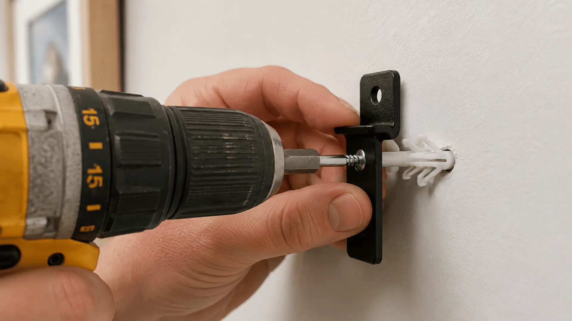 person installing a drywall anchor with a drill screw and small mounting bracket on a wall