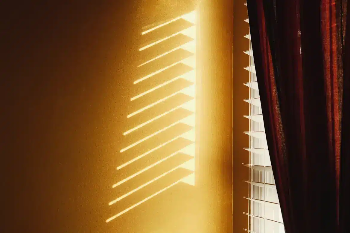 Golden sunlight casting striped shadows through blinds on a warm-toned wall