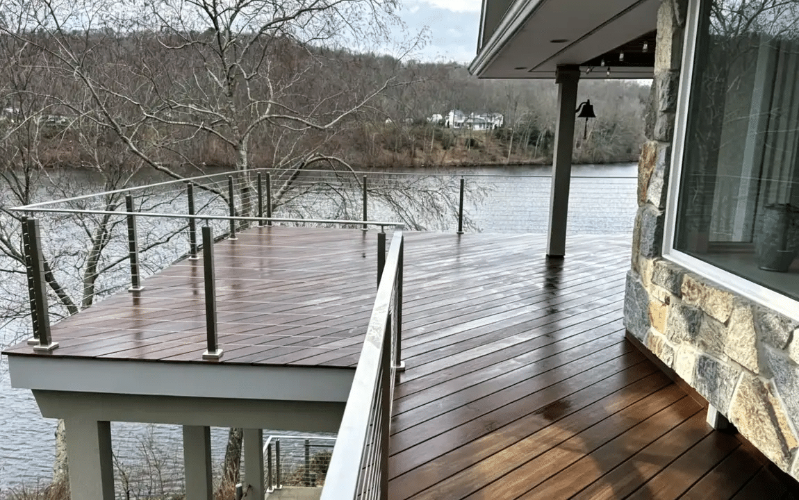Wooden deck overlooking a lake with glass railing and stone exterior wall