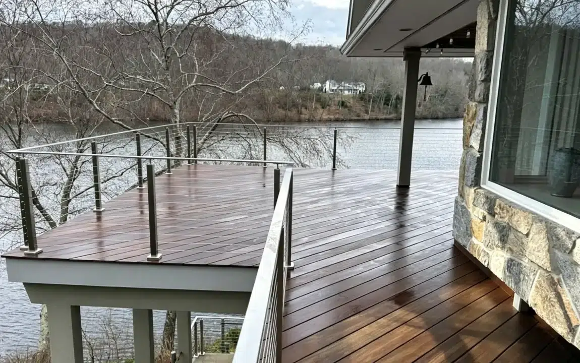 Wooden deck overlooking a lake with glass railing and stone exterior wall