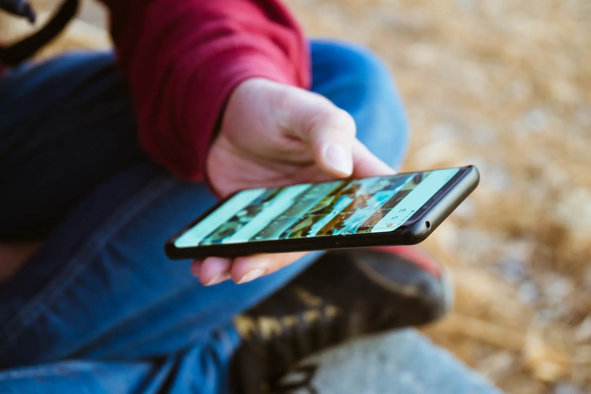 Person holding a smartphone outdoors browsing photos with blurred background