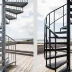 Two spiral staircases, one steel and one black, on a wooden deck overlooking the sea
