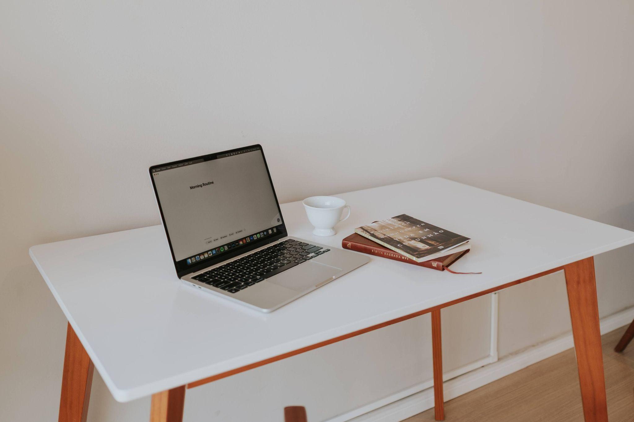 Open laptop on wooden desk next to a cup and books in a minimalist workspace