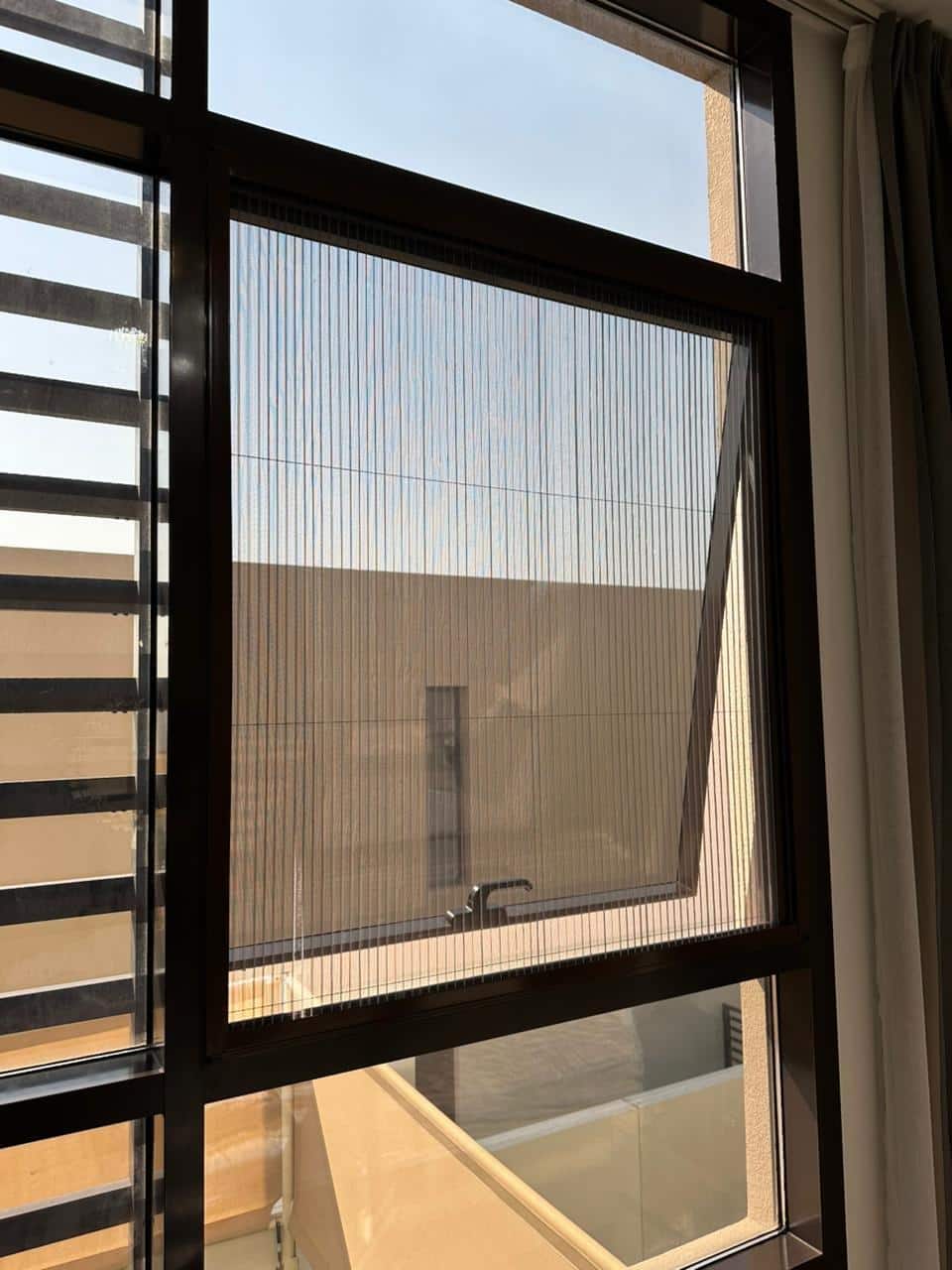 Modern window with pleated screen partially opened in bright sunlit room