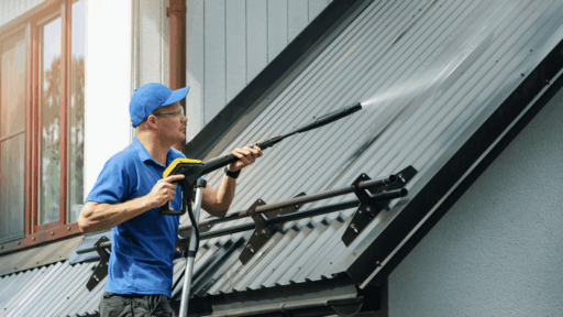 professional using a pressure washing wand to clean a sloped metal roof outside a home
