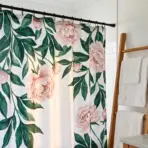 Floral shower curtain with pink peonies in white bathroom featuring wooden towel ladder and potted plant