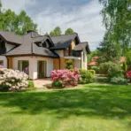 House with dark roof surrounded by blooming pink azaleas in a lush green garden
