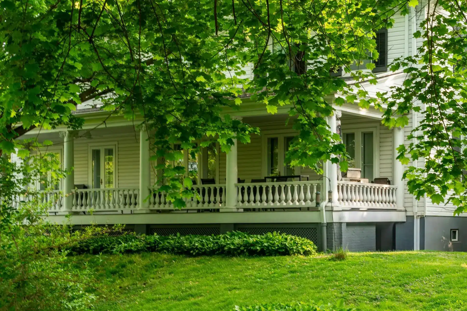 Victorian-style house porch surrounded by lush green trees and grass in a serene setting
