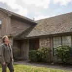 Person inspecting roof of suburban home with wooden siding and brick facade