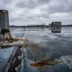Rusty vent pipe and puddles on flat industrial rooftop under cloudy sky