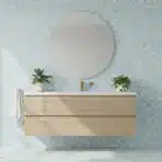 Modern bathroom with round mirror above floating wood vanity, blue hexagonal tile wall, and leafy plants