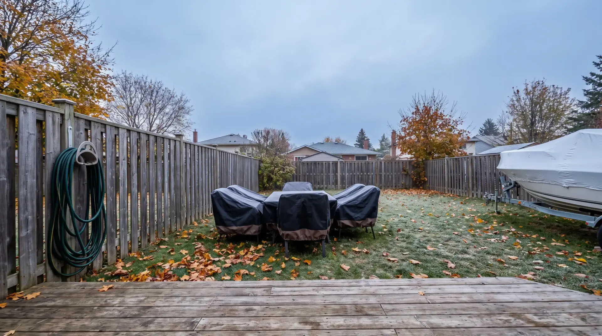 Outdoor patio furniture with protective covers on frosty lawn surrounded by wooden fence in fall setting