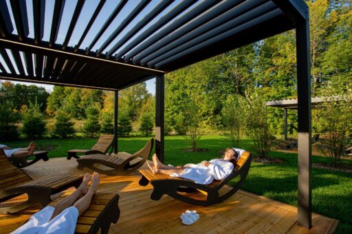 Person relaxing on wooden lounge chair under pergola in sunny garden setting