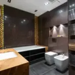 Modern bathroom with wood countertop, tub, and dark tiled walls under warm lighting