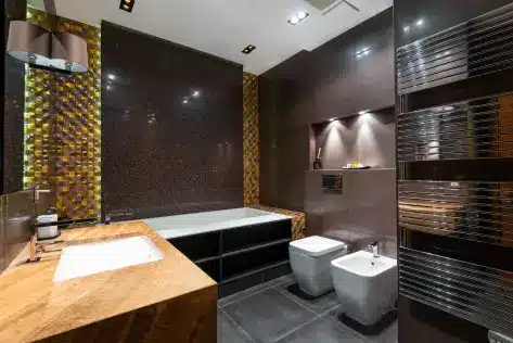 Modern bathroom with wood countertop, tub, and dark tiled walls under warm lighting