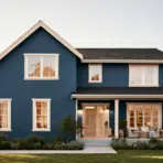 Two-story blue house with white trim surrounded by green landscaping in a suburban setting
