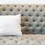 Gray tufted sofa with white patterned pillow against white brick wall backdrop