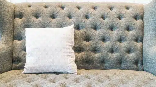 Gray tufted sofa with white patterned pillow against white brick wall backdrop
