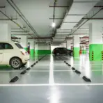 Underground parking garage with parked cars and green-striped columns under fluorescent lighting