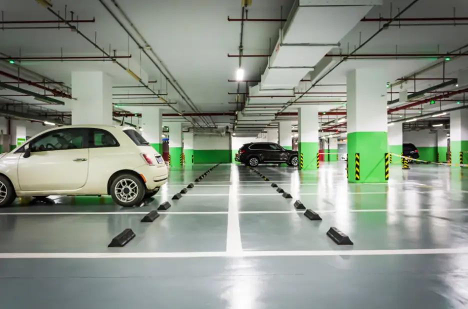 Underground parking garage with parked cars and green-striped columns under fluorescent lighting