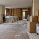 Unfinished living room renovation with stacked cardboard boxes and covered furniture, under soft natural light