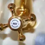 Golden vintage-style hot water tap in bathroom setting with white porcelain sink