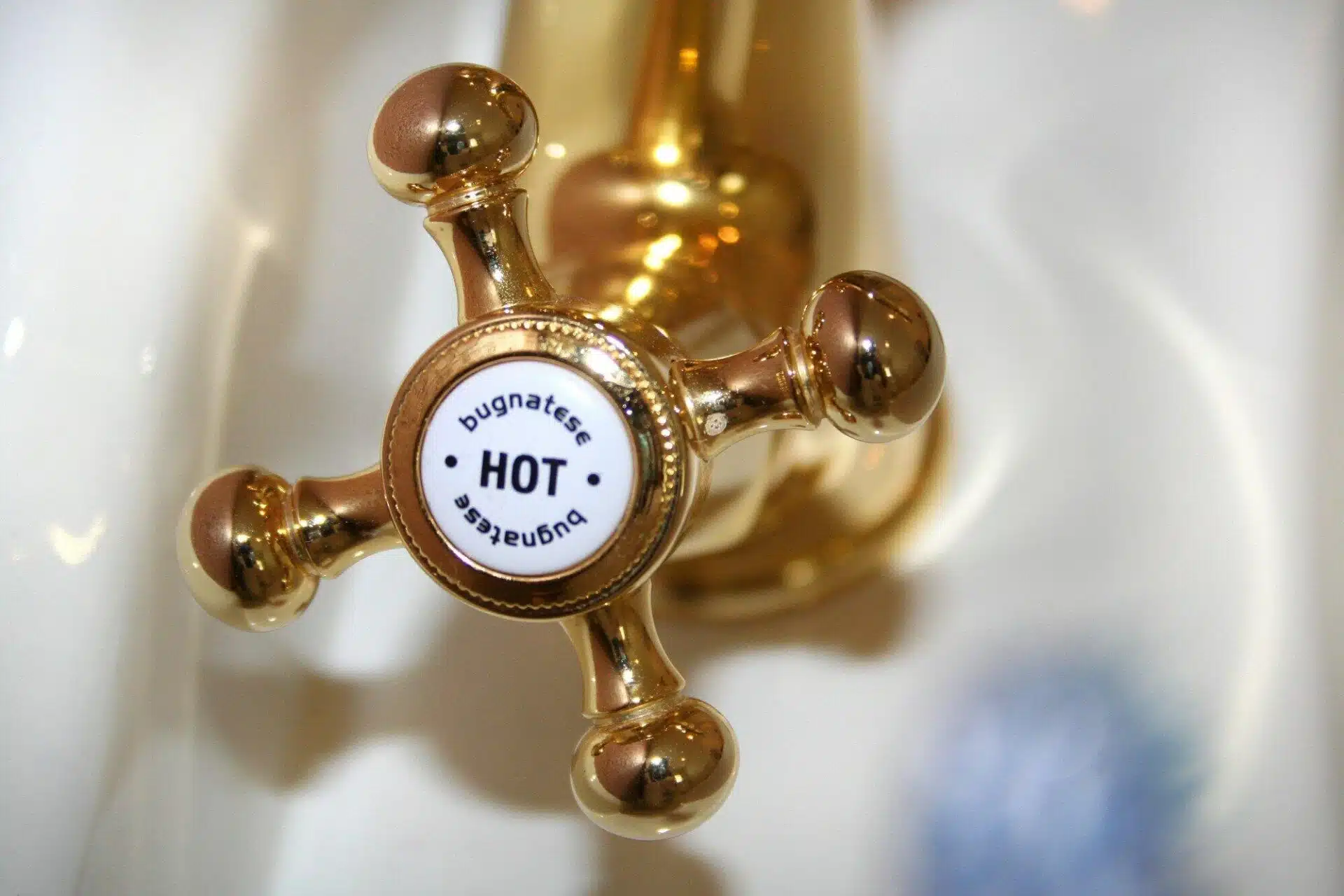Golden vintage-style hot water tap in bathroom setting with white porcelain sink