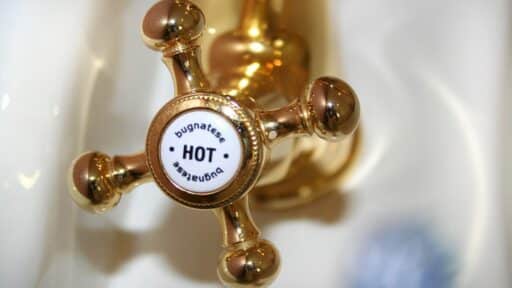 Golden vintage-style hot water tap in bathroom setting with white porcelain sink