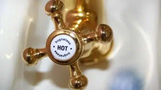 Golden vintage-style hot water tap in bathroom setting with white porcelain sink