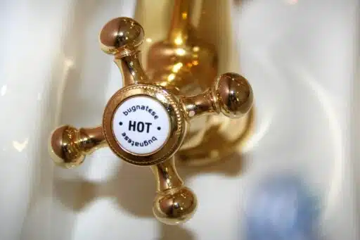 Golden vintage-style hot water tap in bathroom setting with white porcelain sink