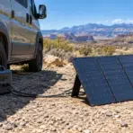 Solar panel setup beside a camper van in a desert landscape under blue skies