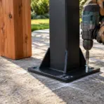 Drilling metal beam base into concrete with power drill outdoors in a garden setting